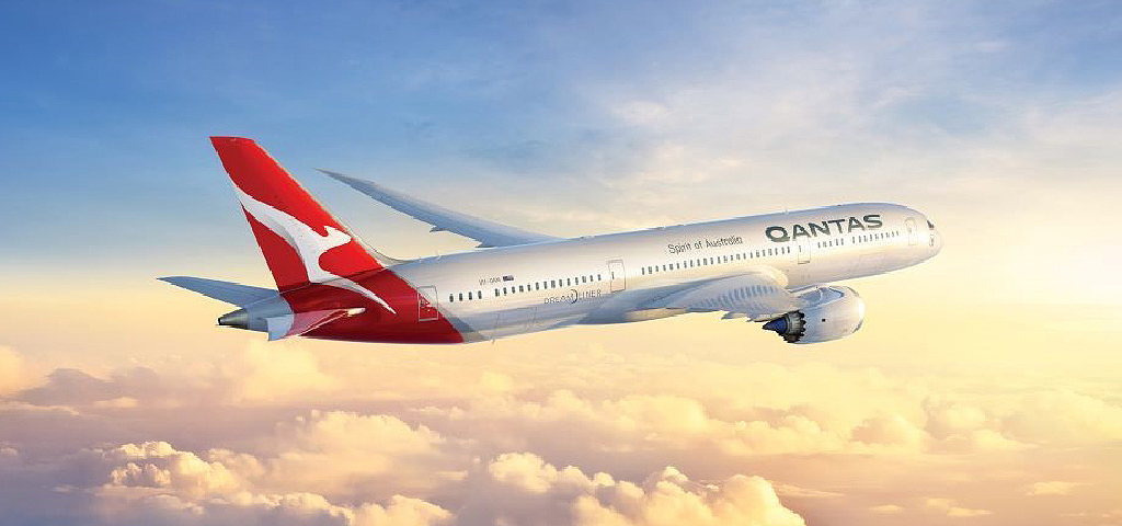 Qantas plane flying through the sky at sunrise.